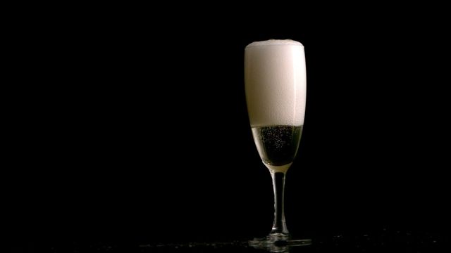 Champagne glass prominently displays bubbling drink with foam on top, set against dark backdrop. Represents celebration, luxury and elegance. Ideal for advertising celebratory occasions, parties, or luxury drinking experiences.