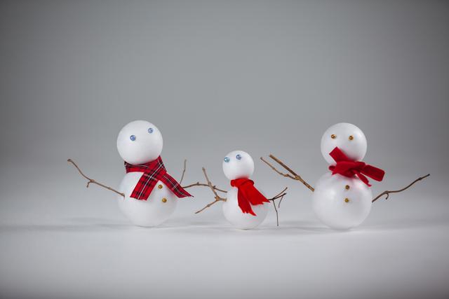 Three snowman ornaments with red scarves are standing against a white background. These festive decorations are perfect for adding a touch of holiday cheer to any setting. Ideal for use in Christmas-themed projects, greeting cards, or winter holiday promotions.