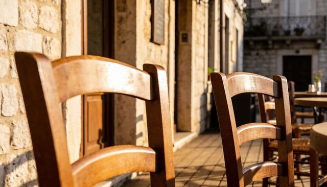 Sunlight warming wooden ladder-back chairs on rustic stone terrace outside cafe
