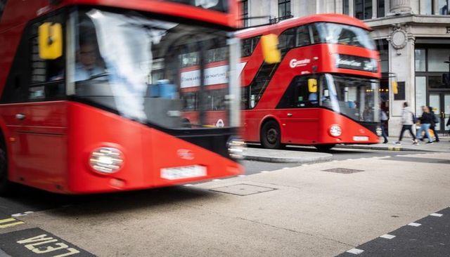 Moving red double-decker buses passing london street, commuters walking, urban motion blur