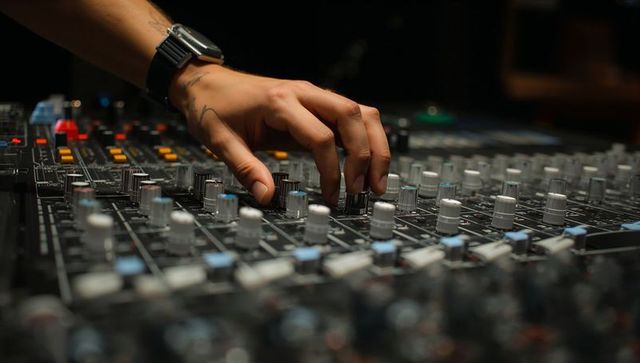 Sound engineer adjusting mixing console knob close-up with wristwatch and tattoos