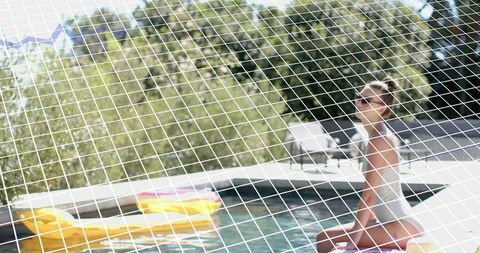 Sitting, relaxing woman in swimsuit with sunglasses by pool with yellow float, grid overlay