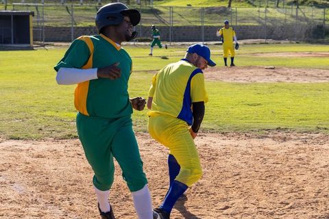 Adult baseball players sprinting and fielding at base during amateur league game