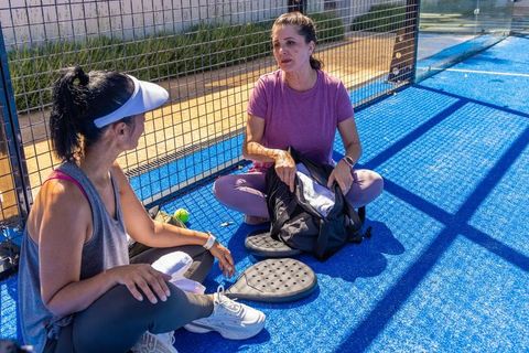 Diverse women chatting and unpacking bags on sunny blue pickleball court