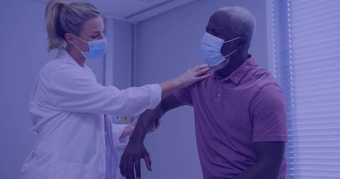 Female doctor examining male patient shoulder mobility in clinic, wearing masks
