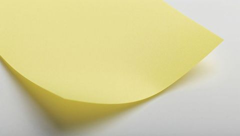 Curled yellow sticky note on white surface with soft shadow and paper texture
