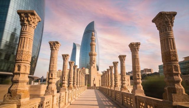 Carved stone bridge leading to minaret with reflective glass towers at sunset skyline