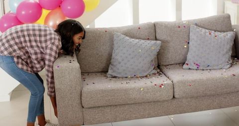 Woman sweeping confetti off sofa in living room cleanup