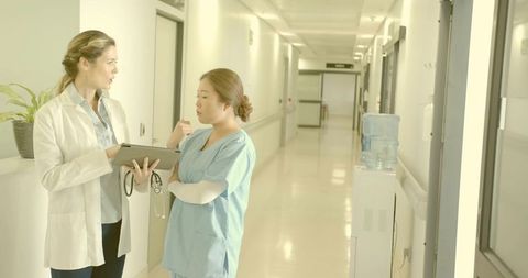 Doctor and Nurse Discussing Patient Care on Tablet in Hospital Corridor