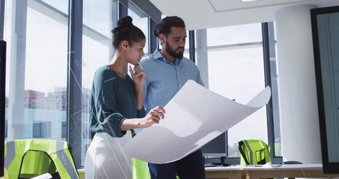 Architects examining large blueprint in modern office with lime-green safety vests