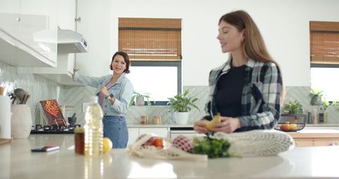 Diverse female friends preparing fruit at modern kitchen island with reusable produce bag