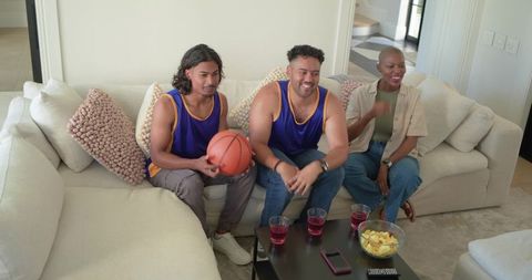 African american friends watching basketball game on sofa with snacks and drinks
