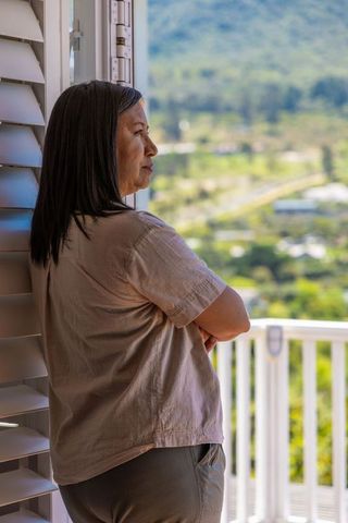 Mature woman standing in doorway gazing over sunlit valley from balcony