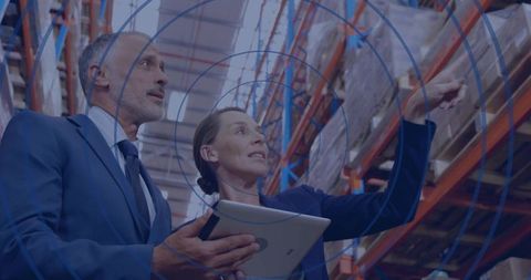 Warehouse managers reviewing inventory with tablet by pallet racks for logistics analytics