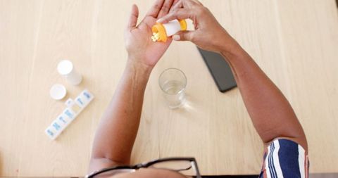 Senior woman taking medication at home with pills and glass of water