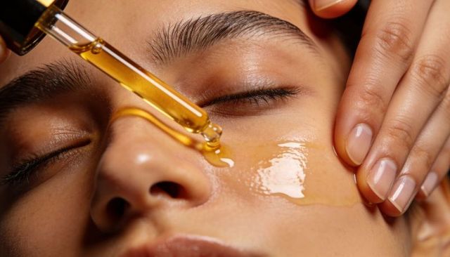Golden facial serum droplet on closeup female face applying skincare oil for glowing skin
