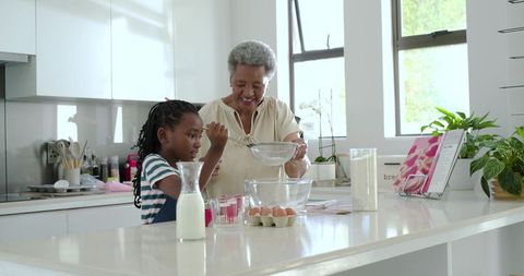 Grandparent and child baking together in bright modern kitchen, sifting and stirring