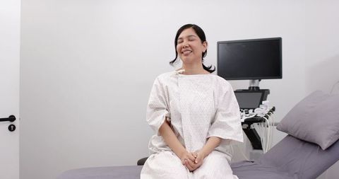 Smiling patient sitting on exam table in hospital gown with ultrasound monitor