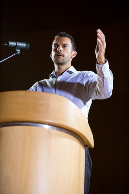 Business executive stands at podium and gives a speech at a conference. Ideal for use in articles or promotions about corporate events, leadership conferences, business seminars, or public speaking workshops.