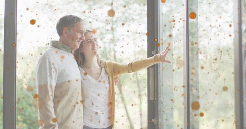 Teen daughter pointing outside while embracing father by speckled glass door