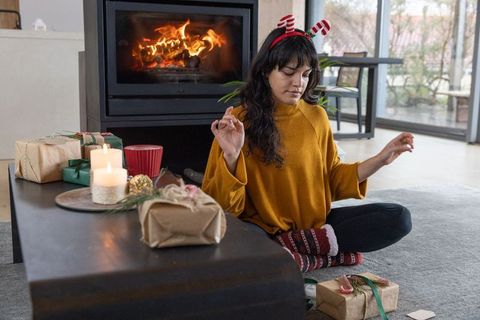 Woman meditating in cozy festive living room by fireplace