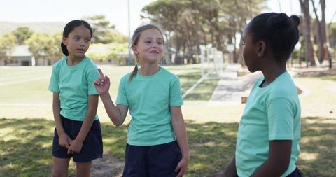 Diverse girls soccer teammates talking, laughing and bonding on sunlit school sports field