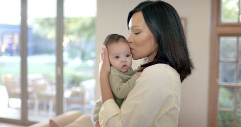 Motherly bond: mother cradles and kisses infant in cozy living room