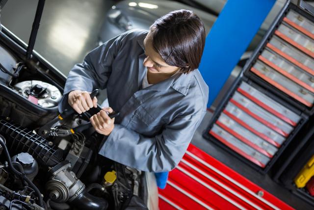 Female mechanic working on car engine in an auto repair garage. Ideal for illustrating automotive services, gender diversity in the workplace, and professional car maintenance. Suitable for use in advertisements, websites, and articles related to car repair, automotive industry, and skilled trades.