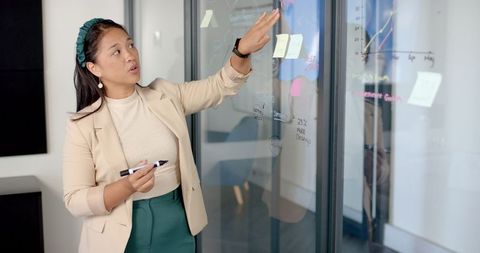 Confident Businesswoman Presenting Data on Glass Board in Modern Office