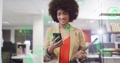 Black professional checking phone holding tablet with sustainability tech icons in office