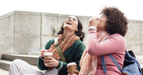 Friends laughing together while enjoying takeaway coffee on city steps