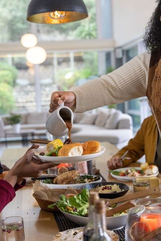 Family gathering pouring gravy over dinner rolls and corn during cozy home feast together