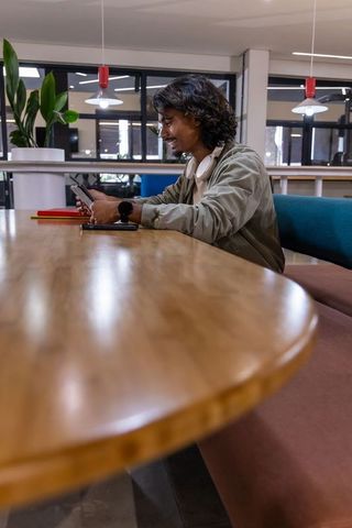 Young asian man checking smartphone at communal coworking table with headphones