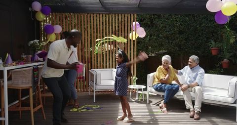 Multigenerational family celebrating birthday on sunlit backyard deck under pergola