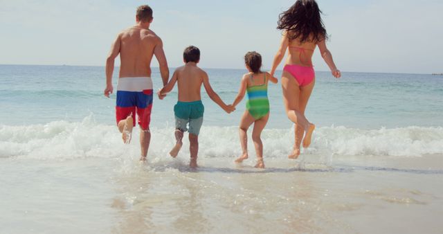 Family of four running into ocean waves on a sandy beach holding hands. Father, mother, and two children joyfully entering water in swimwear. This image can be used to illustrate concepts of family bonding, summer vacation, outdoor activities, and carefree enjoyment. Ideal for travel brochures, family-oriented advertisements, and lifestyle magazines.