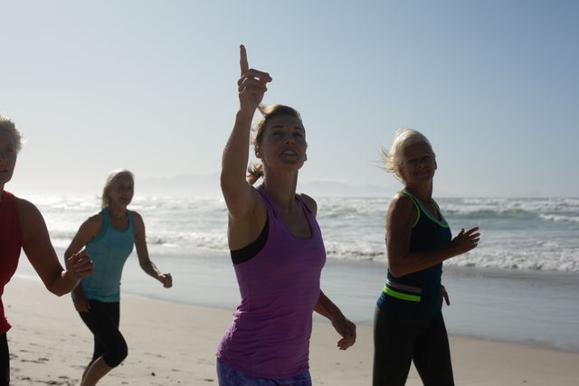 Group of Caucasian female friends enjoying exercising on a beach on a sunny day, running on the seashore and smiling.