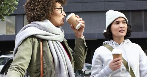 Friends Sipping Takeaway Coffee While Walking Urban Street on Chilly Overcast Morning