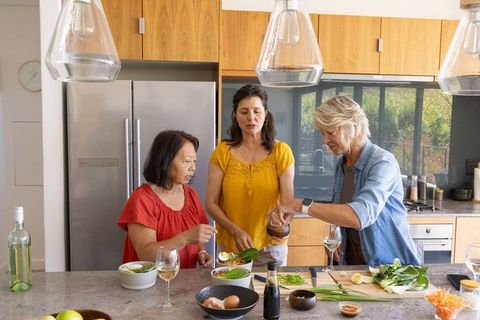 Diverse women preparing healthy bowls at kitchen island, sharing cooking and wine together
