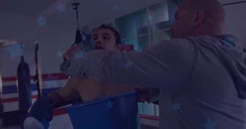 Exhausted boxer catching breath in ring corner while coach hands water from blue bucket