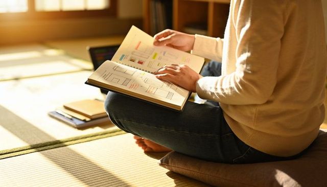 Woman reading sketchbook on tatami floor with zabuton cushion in warm morning sunlight