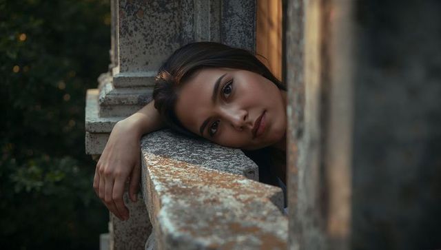 Young woman leaning on weathered stone balustrade gazing in golden hour light