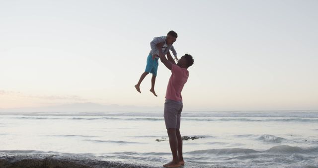 African american father carrying his son on sunny beach. healthy and active time beach holiday.
