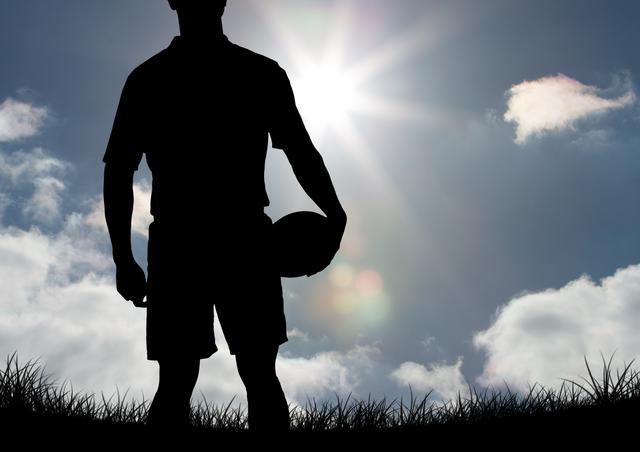 Silhouette showing soccer player standing on grassy field with ball in hand, bright sun in sky with clouds in background. Ideal for sports-related advertisements, motivational posters, and athletic event promotions, emphasizing determination, readiness, and the competitive spirit.