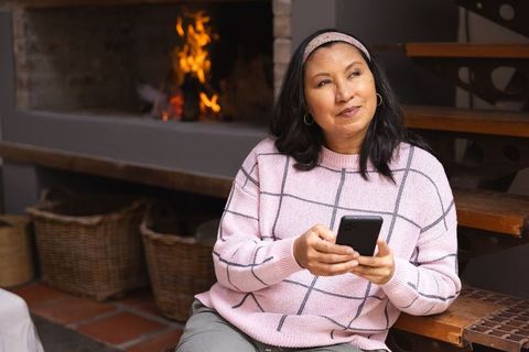 Middle-aged woman relaxing with smartphone by fireplace