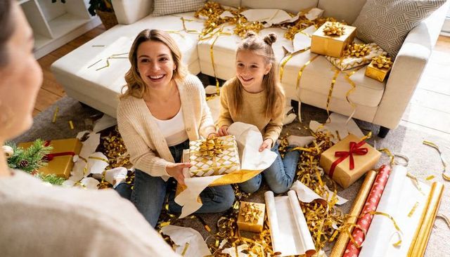 Mother and daughter unwrapping holiday gifts on living room rug, smiling, cozy celebration