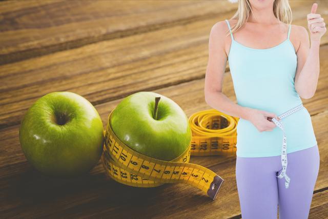 Digital composite of Midsection of woman showing thumb up while measuring waist by fruits and nuts