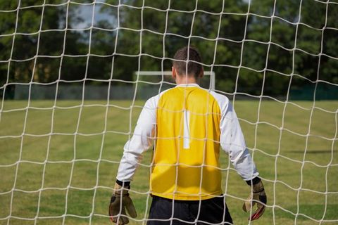 Goalkeeper anticipates game in goal net on sunny soccer field