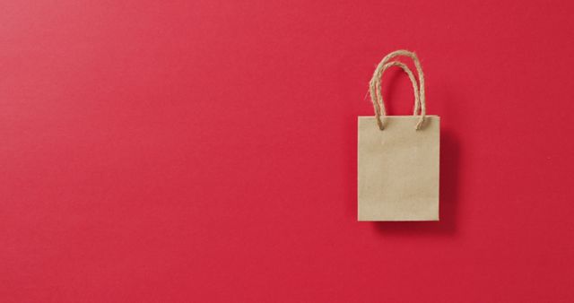Small brown gift bag with string handles on red background with copy space. Shopping, sale and retail concept digitally generated image.