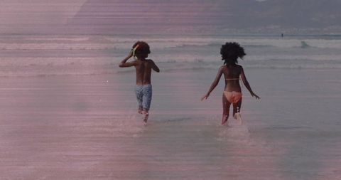 Two kids running into shallow ocean water at beach wearing snorkel and colorful swimwear