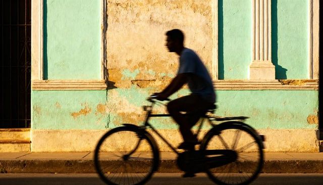 Silhouette cyclist riding past weathered teal wall at golden hour street scene